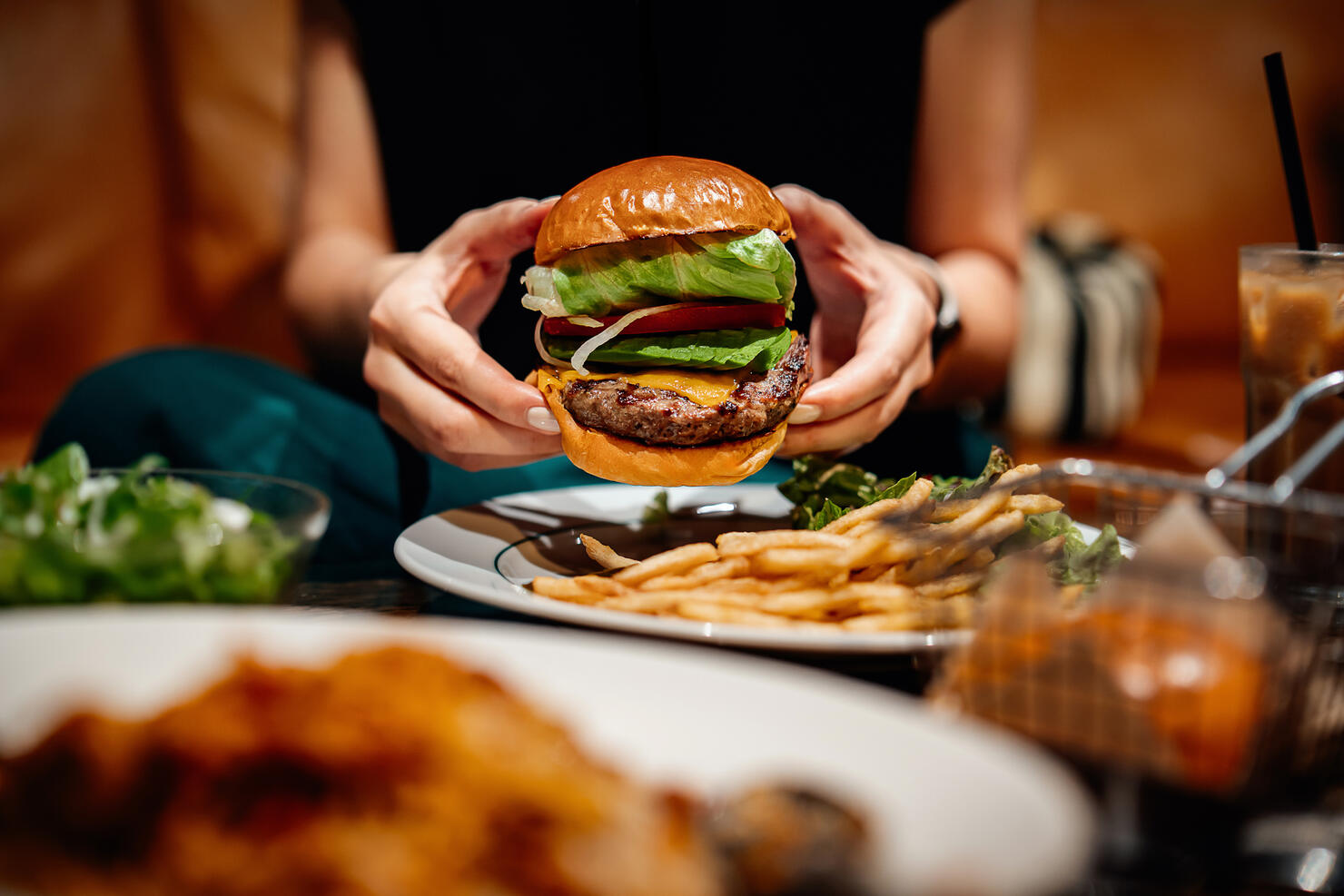 Cropped shot, mid-section of young Asian woman eating freshly made delicious avocado burger with fries on the dining table. Enjoying a feast in the restaurant. Dining out. People, food and lifestyle