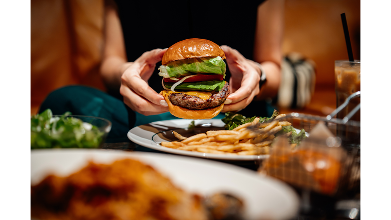 Cropped shot, mid-section of young Asian woman eating freshly made delicious avocado burger with fries on the dining table. Enjoying a feast in the restaurant. Dining out. People, food and lifestyle