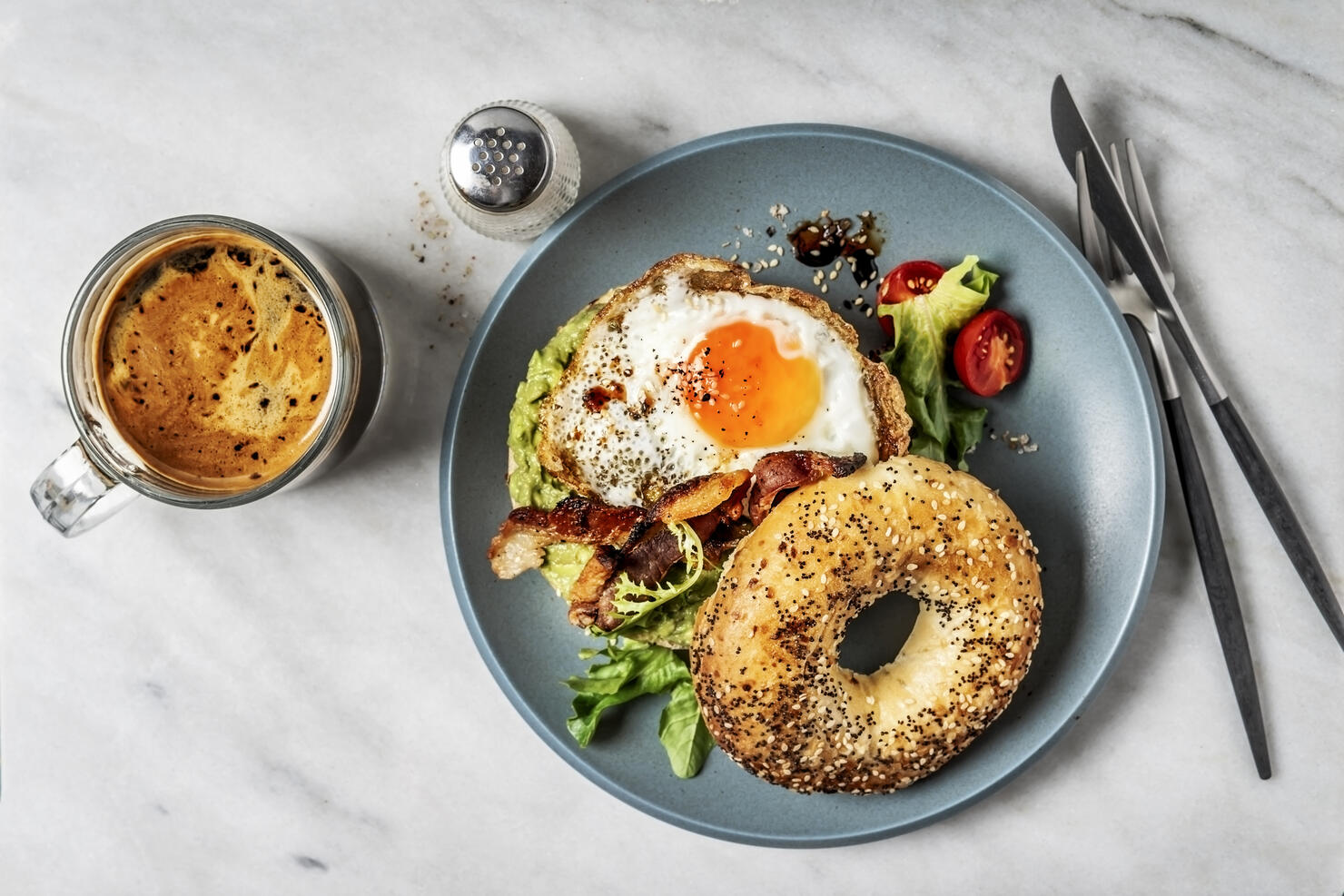 Bagel sandwich with avocado, fried egg and side salad on white background