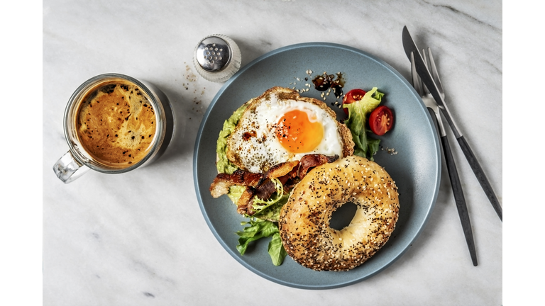 Bagel sandwich with avocado, fried egg and side salad on white background
