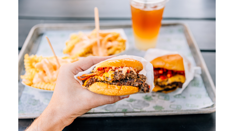 Person eating double cheeseburger with bacon at a fast food joint, personal perspective view