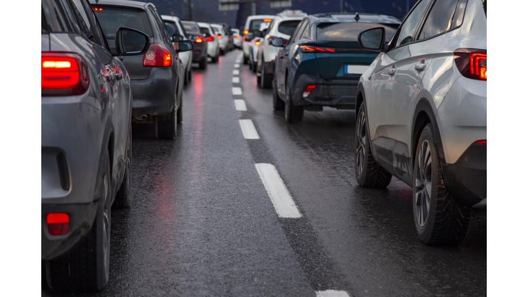 Traffic jam with a row of cars on a highway during rush hour in the evening after work. red brake lights of stopped cars on the background of wet asphalt with white lanes at sunset