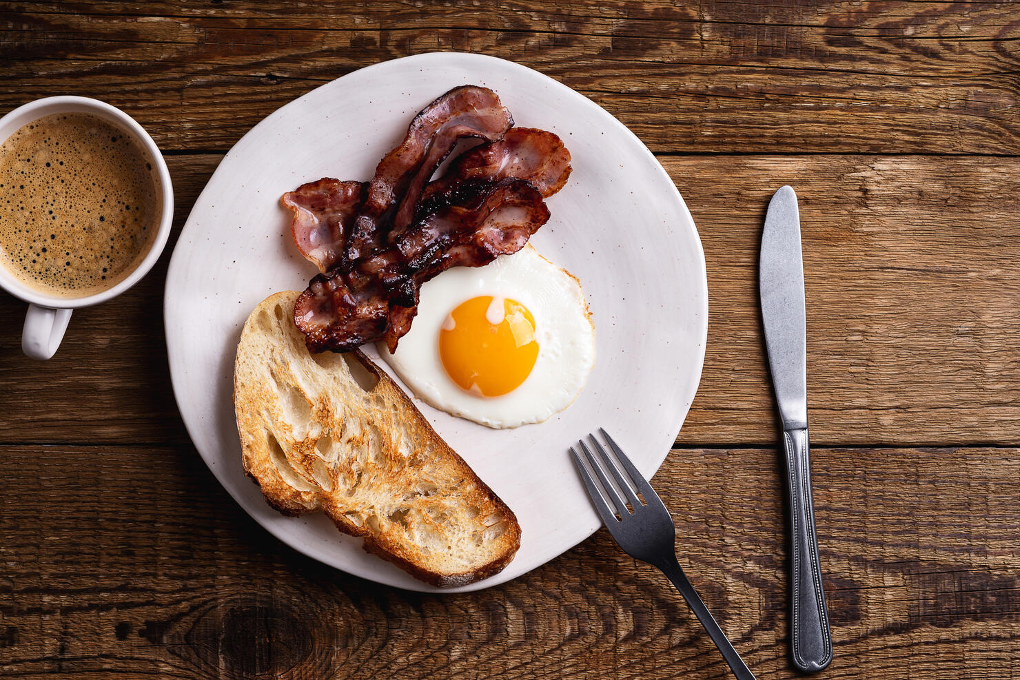 Breakfast on ceramic plate. Fried egg, bacon, toasted bread and mug of coffee