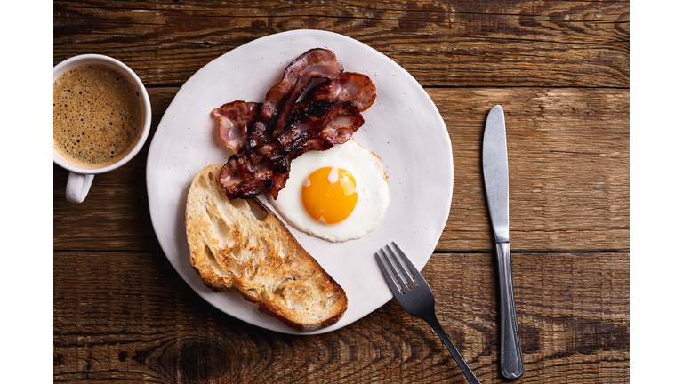 Breakfast on ceramic plate. Fried egg, bacon, toasted bread and mug of coffee
