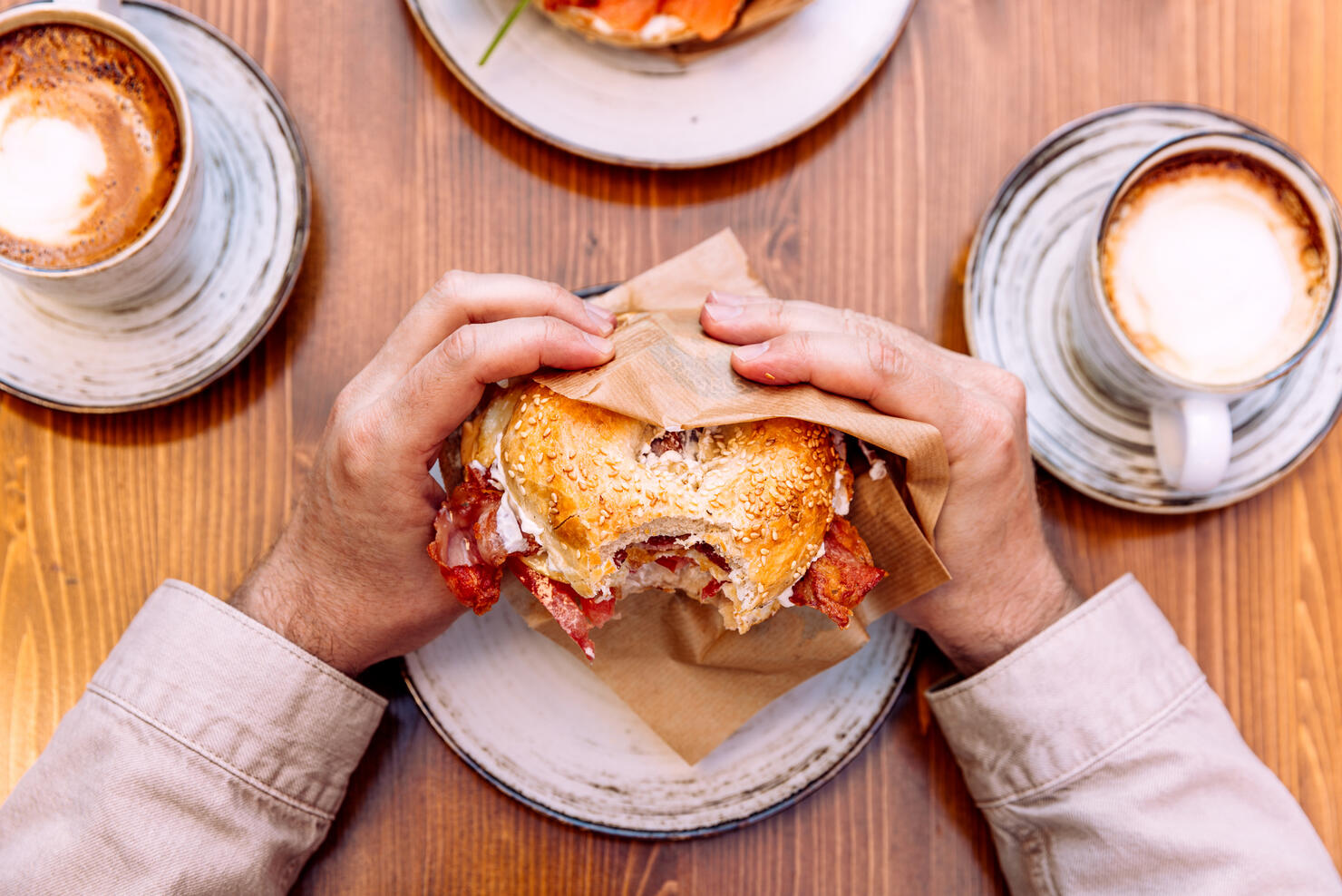 Man eating bagel with bacon, cream cheese and fried egg, personal perspective view