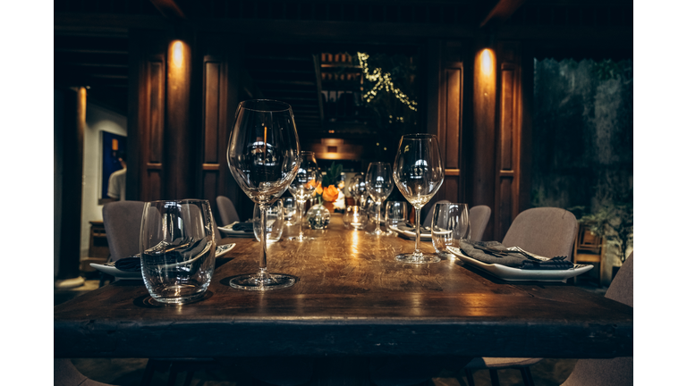 Elegant table setting in fine dining room. Beautifully set dining table with wine glasses in a dimly lit, upscale house.
