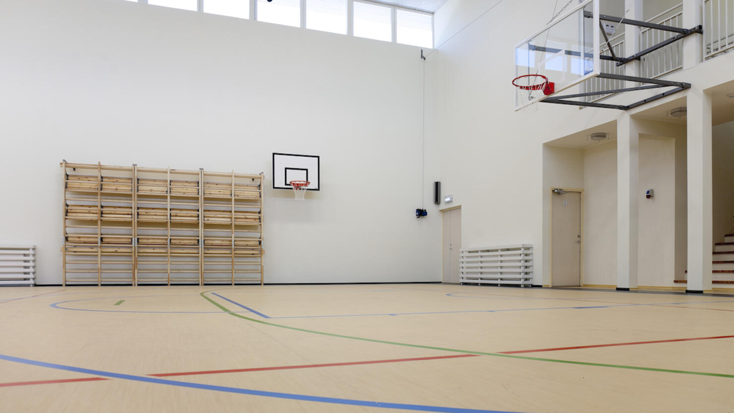 Indoor basketball court at a school. Wooden floor and marked court, a hoop and backboard