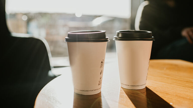Takeaway coffee cups on a wooden table casting long shadows