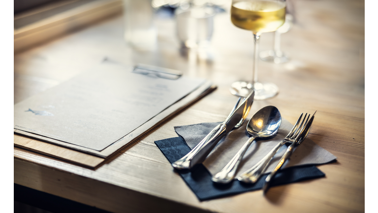 Cutlery on a table in a restaurant, a table set and a menu for a customer placed next to it.