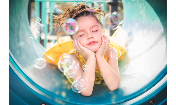 beautiful junior little girl playing in the park in yellow dress laughing with bubbles, screaming with happiness in family enjoying children's day