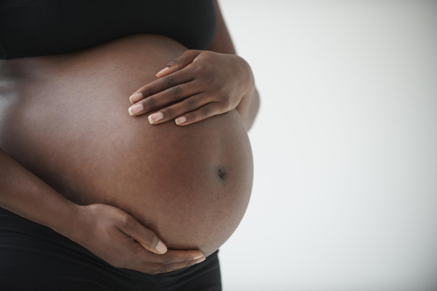 Midsection of pregnant Black woman holding belly