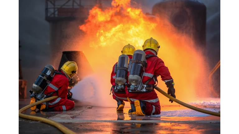 Professional team firefighter supporting their team and spraying the high-pressure water to fire at the base of fire in the pipe tube, Safety disaster accident and public service concepts.